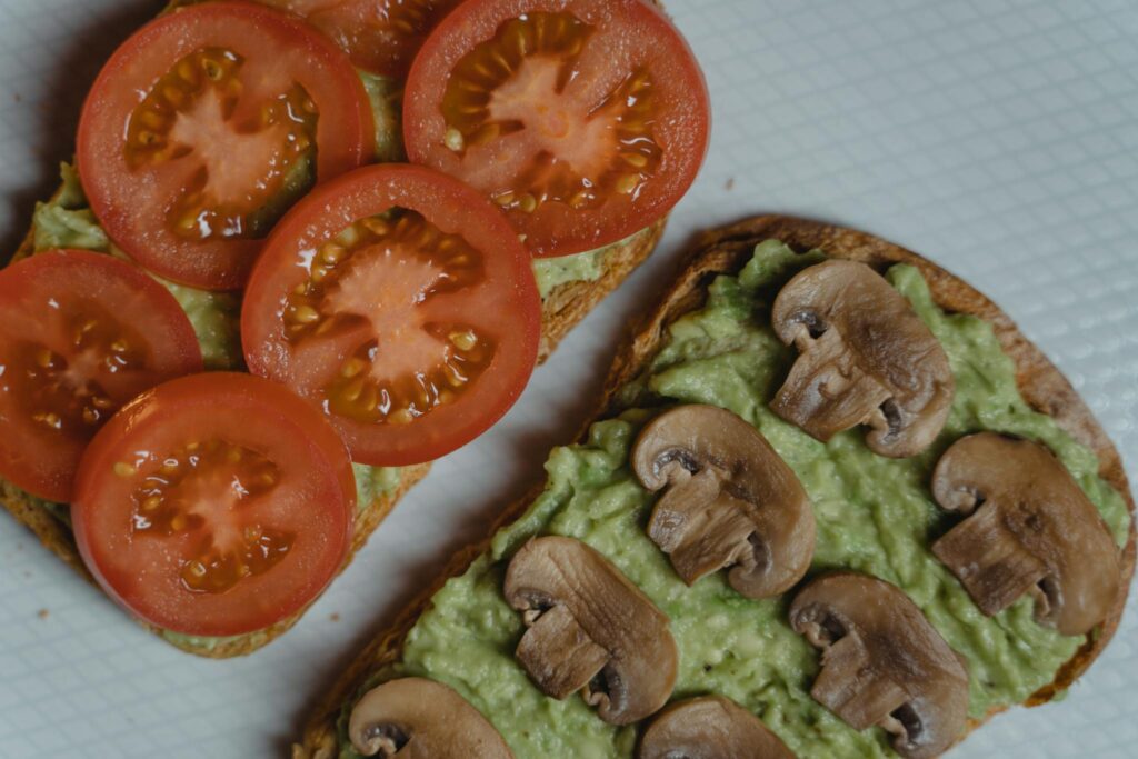 Close-up of avocado toasts topped with fresh tomatoes and mushrooms, a healthy vegan snack.