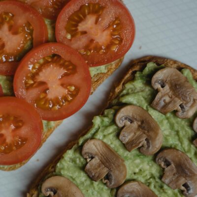 Close-up of avocado toasts topped with fresh tomatoes and mushrooms, a healthy vegan snack.