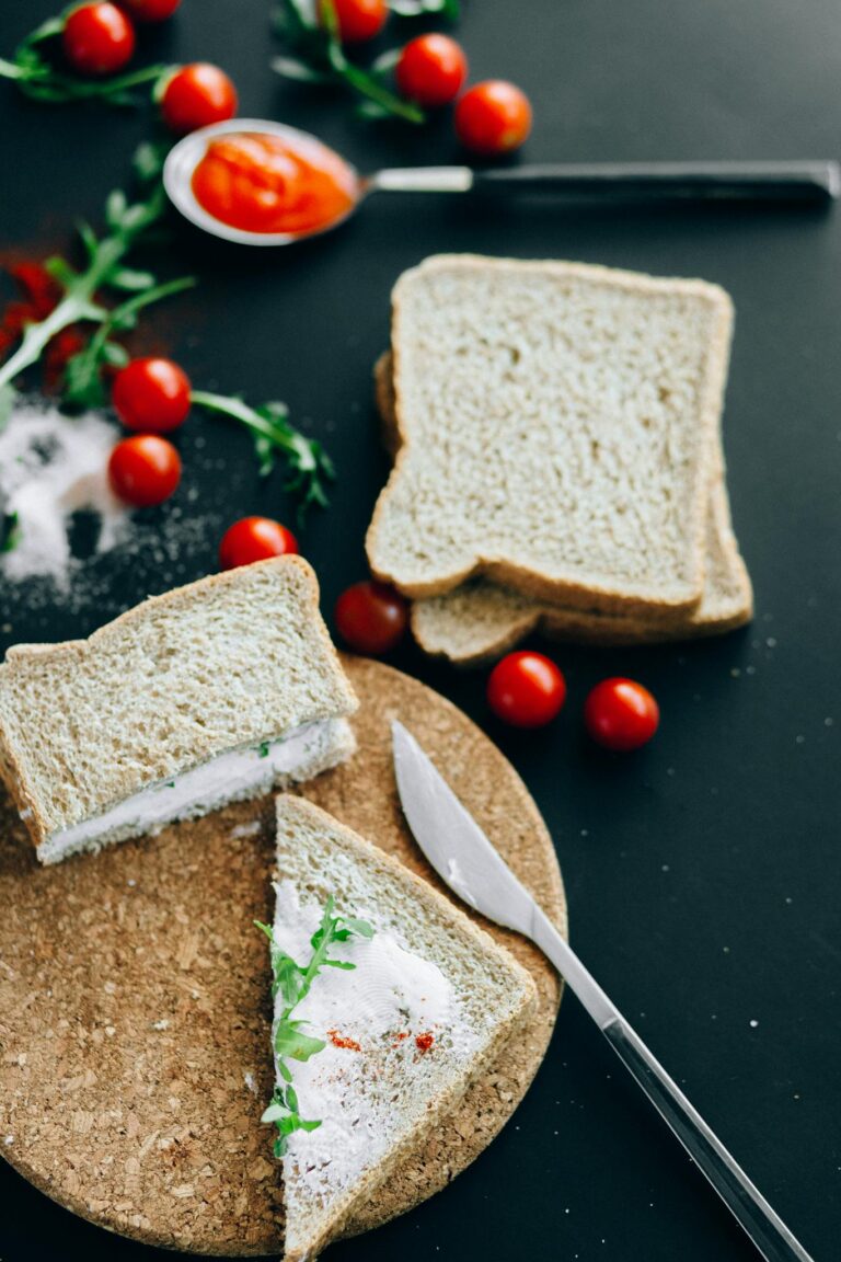 Close-up of sandwich with cream cheese, arugula, and cherry tomatoes on a black background.